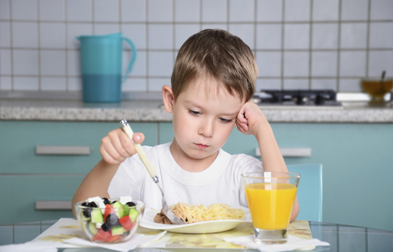 sad little boy sits at the dining table and looking in the plate. horizontal