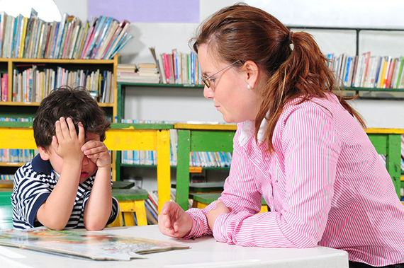 Preschool teacher sitting with student in a classroom.