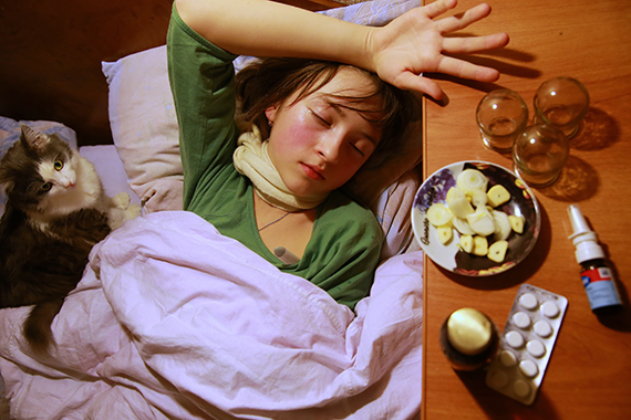 Ребенок, больной гриппом, лежит в кровати рядом с различными лечебными средствами 