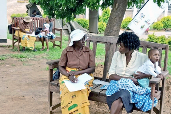 Молодые африканские мамы сидят на скамейках и разговаривают с бабушками