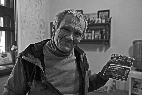 Пожилой мужчина улыбается и показывает пакет тушенки