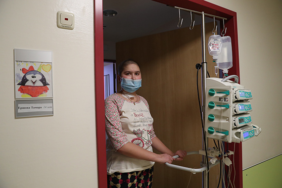 Девушка, больная лейкозом, в дверях палаты с медицинским штативом