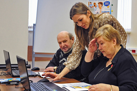 Женщина помогает людям пожилого возраста на уроке компьютерной грамотности
