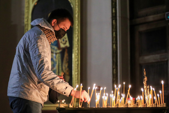 Молодой человек в маске ставит свечу в Казанском кафедральном соборе