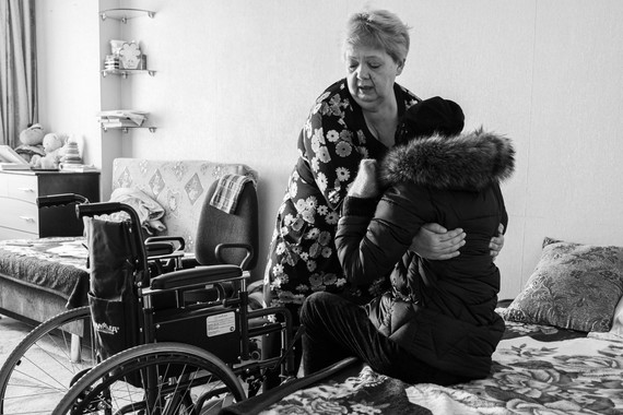 Женщина помогает инвалидке пересесть с кровати в инвалидное кресло