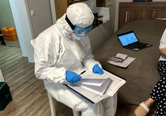 Медицинский работник в защитном костюме в доме у пациента разбирается с документами