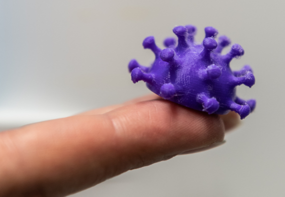 Напечатанная на 3D принтере модель вируса лежит на пальце руки