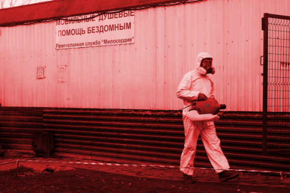 Сотрудник в защитном костюме идет на фоне ангара для бездомных с оборудованием для дезинфекции 