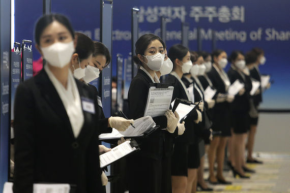 Работницы в масках стоят в ряд на собрании акционеров в Корее