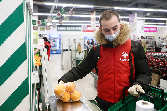 Волонтер в магазине взвешивает апельсины