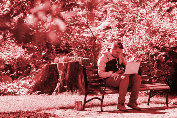 Мужчина с ноутбуком сидит на лавке в парке