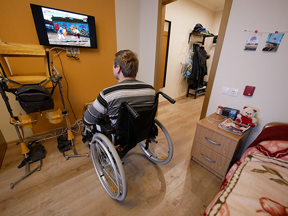 Молодой человек в инвалидном кресле смотрит телевизор