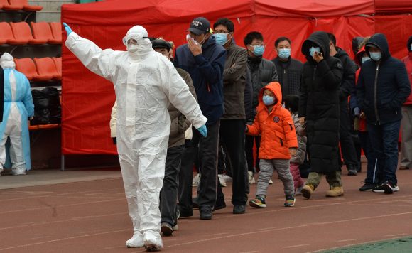 На улице человек в защитном костюме ведет за собой группу китайцев