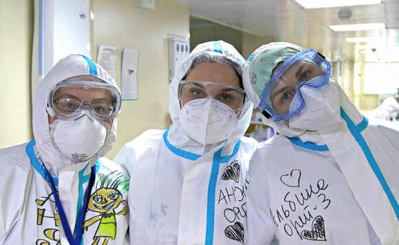 В коридоре больницы три волонтера в защитных костюмах, масках, очках