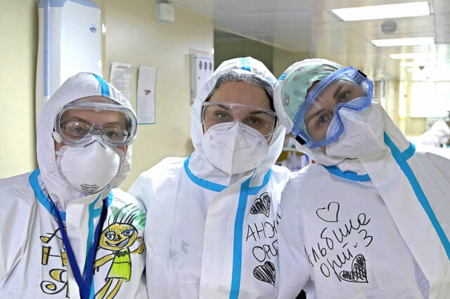 В коридоре больницы три волонтера в защитных костюмах, масках, очках
