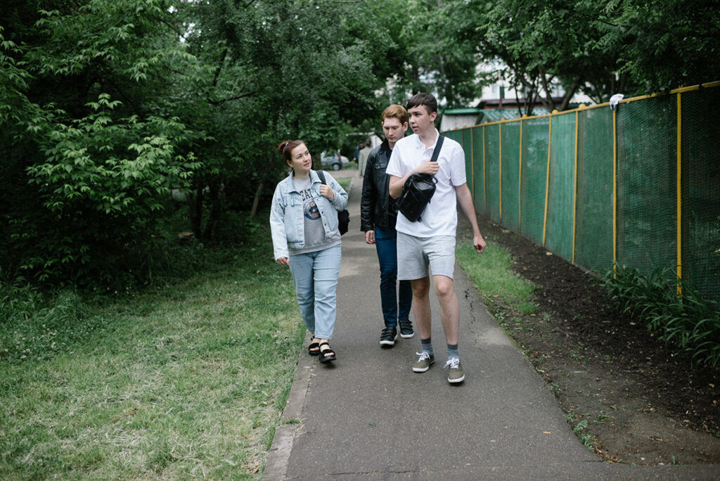 Молодые люди с аутизмом и их тьютор идут по тротуару