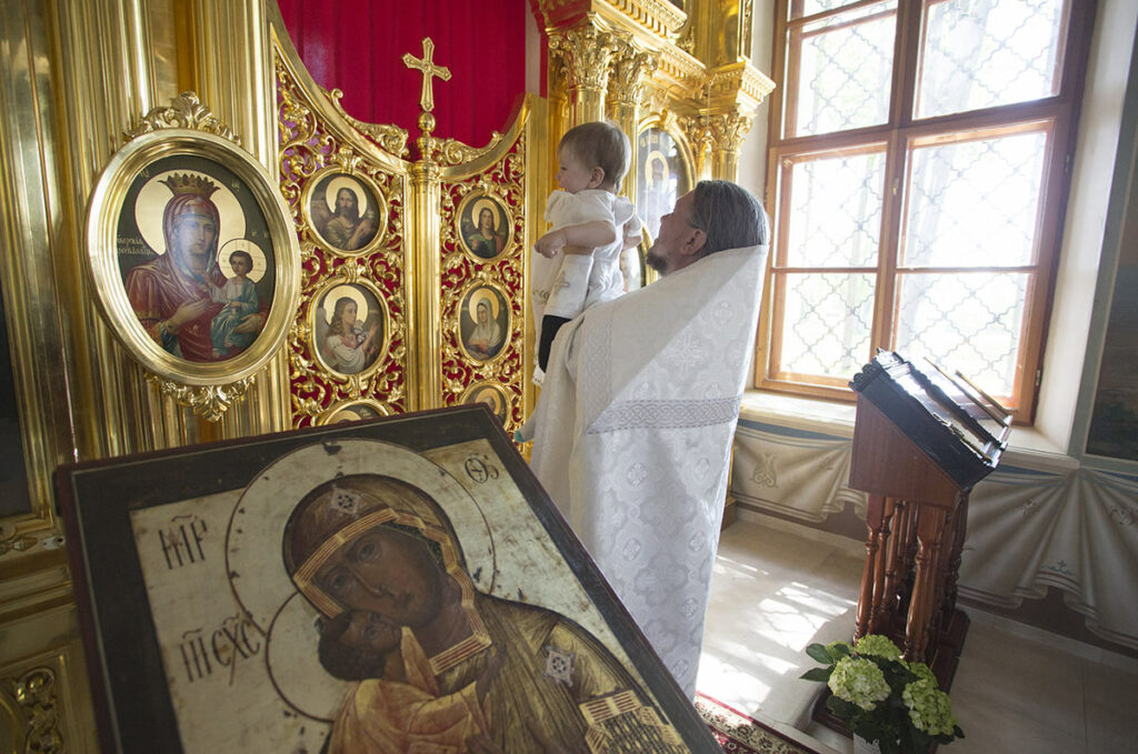 Таинство крещения в Русской православной церкви. Священник держит перед Царскими вратами младенца 