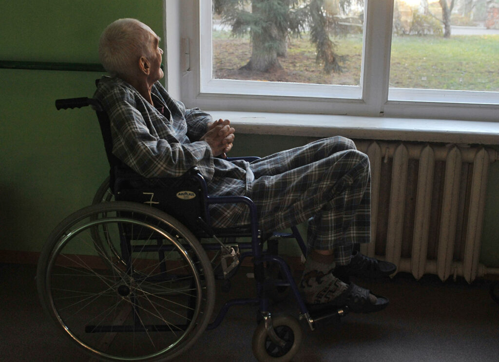 Пациент в инвалидной коляске у окна в психосоматическом отделении психиатрической больницы