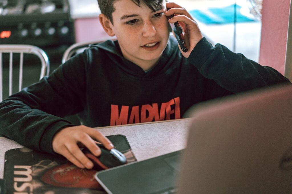 Мальчик разговаривает по телефону и смотрит в ноутбук