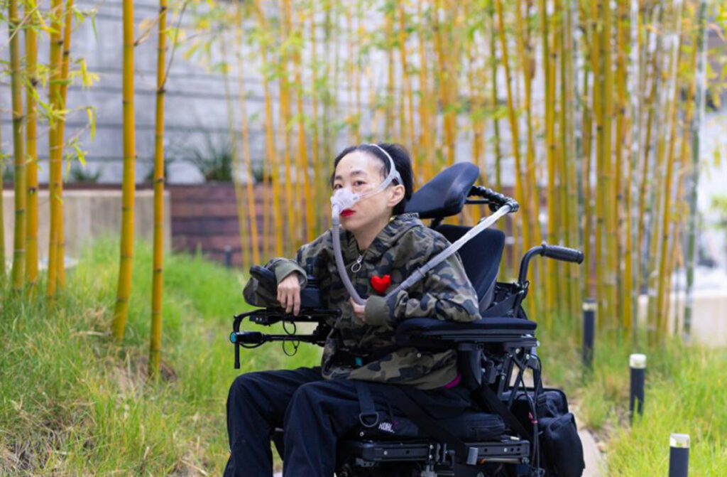 Элис Вонг с трахеостомой в инвалидном кресле