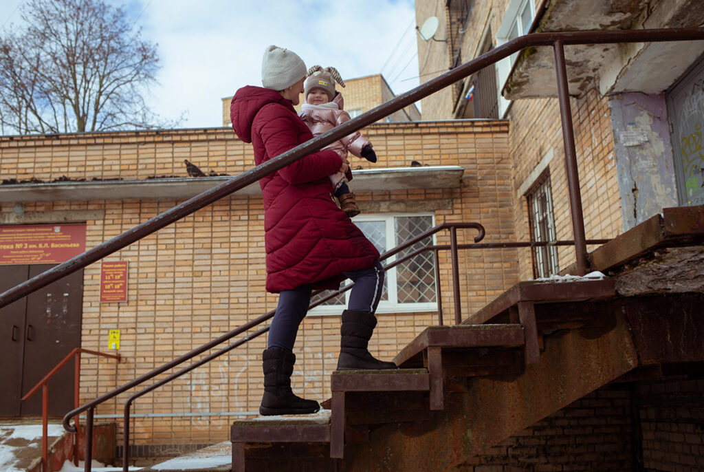 Женщина с маленькой девочкой на руках поднимается по подъездной лестнице