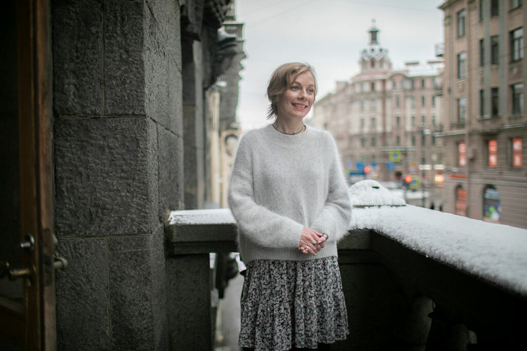 Юлия Корсунская в светлом свитере на балконе здания