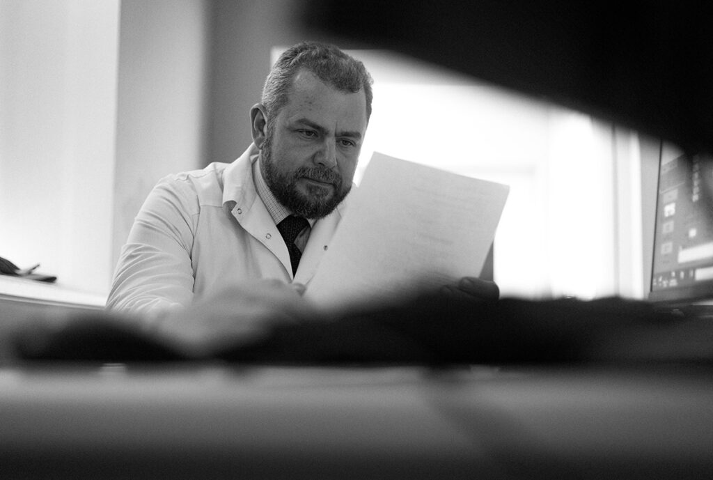 Черно-белая фотография. Алексей Заров за столом читает документацию. 