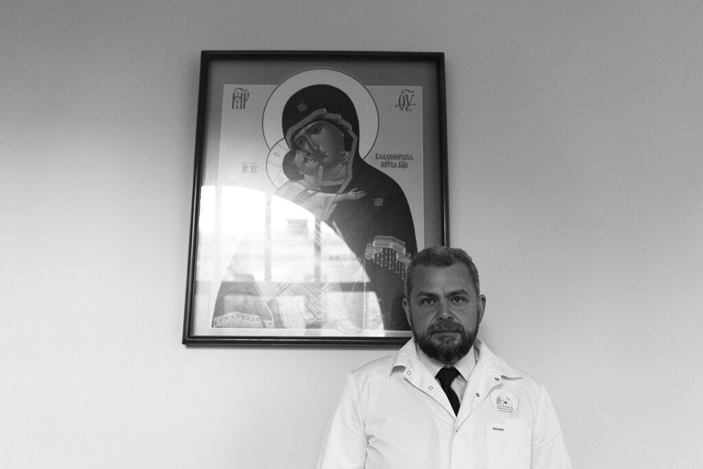 Черно-белая фотография. Алексей Заров на фоне стены с иконой