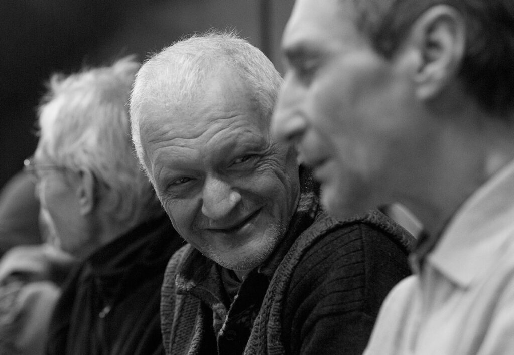 Черно-белая фотография. Трое мужчин, сидящий в середине улыбается