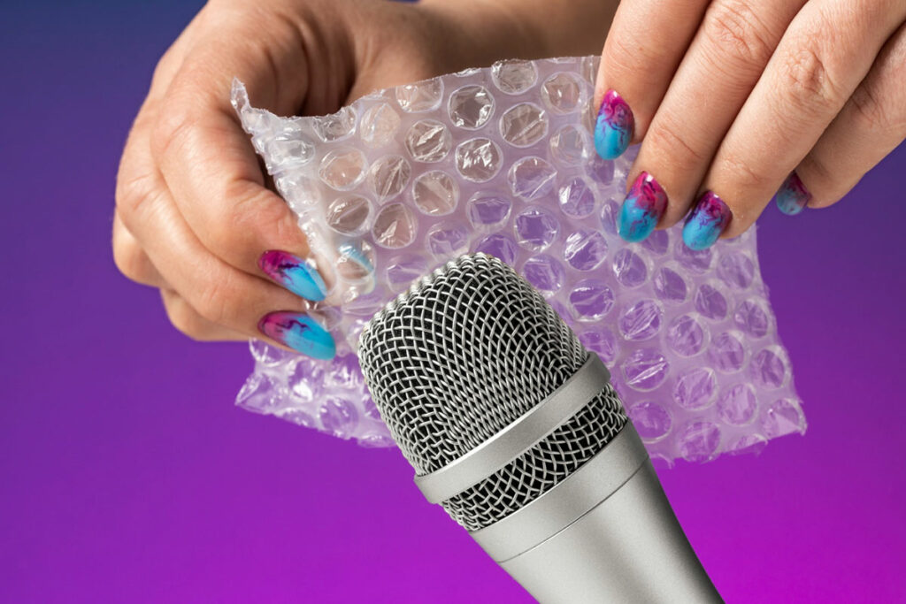 Микрофон и пальцы с ярким маникюром, которые лопают пузырьки на пленке 