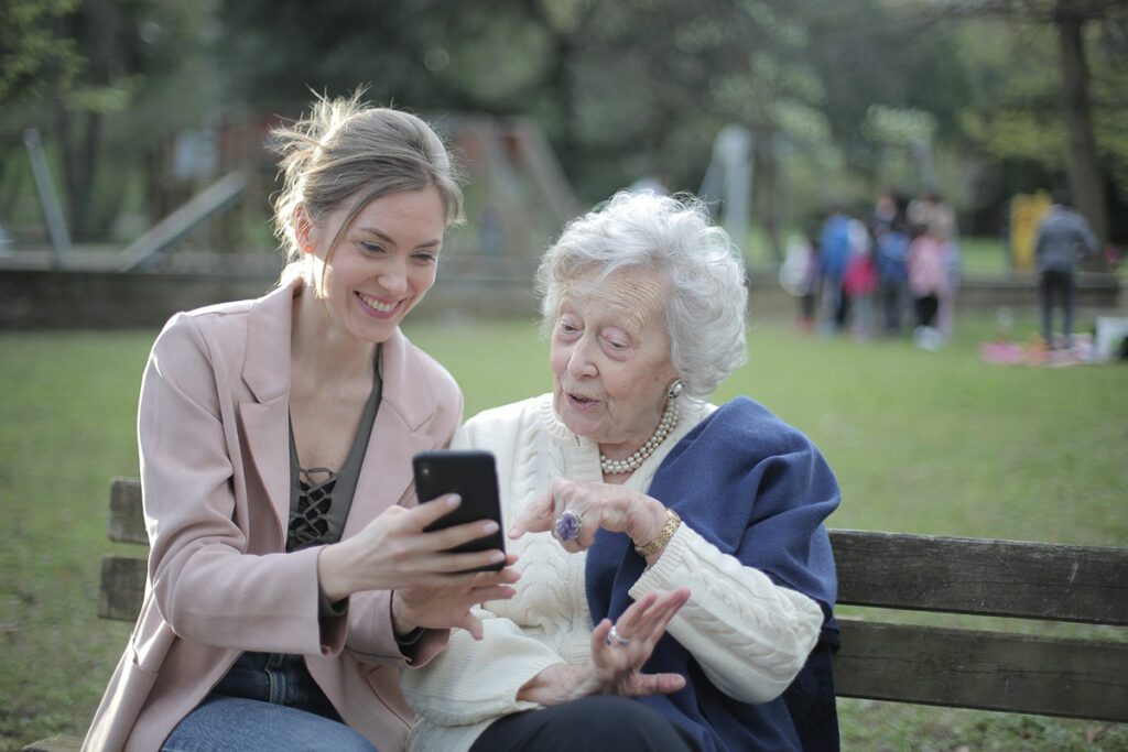 Молодая и пожилая женщины на скамейке в парке смотрят в телефон