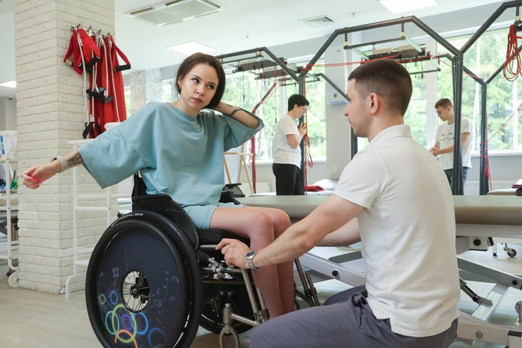 Наташа с инструктором в реабилитационном центре на инвалидной коляске