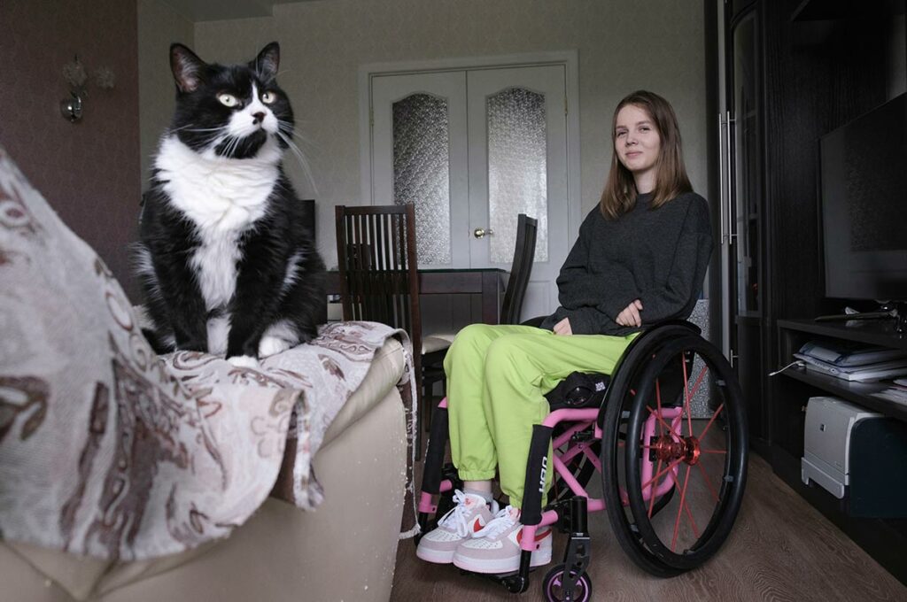 Настя в комнате на инвалидном кресле, на переднем плане кошка