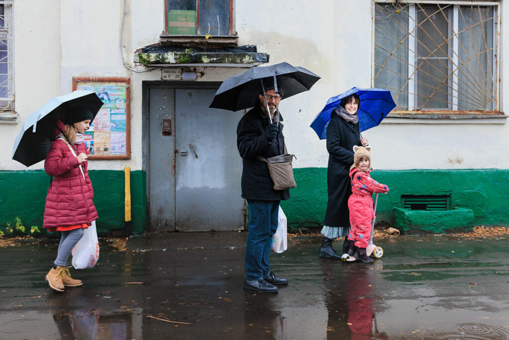 Семья под зонтиками у подъезда дома