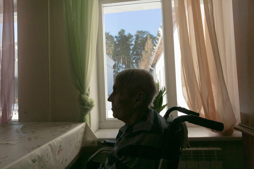 Пожилая женщина в инвалидной коляске на фоне окна в контровом свете