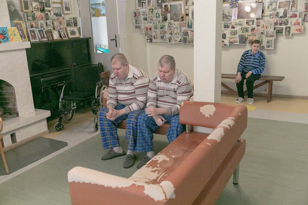 Двое больных мужчин в одинаковых одеждах сидят на диванчике 