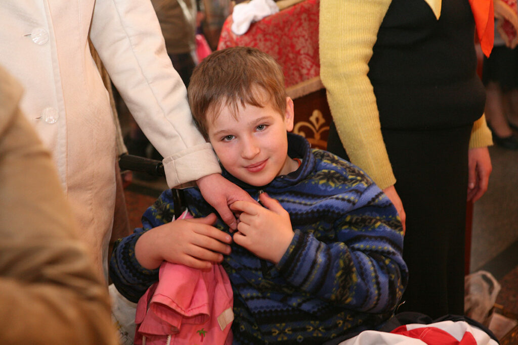 Мальчик в инвалидной коляске держит за руку женщину. Дети из детского дома в храме в Переделкино, 2010 год