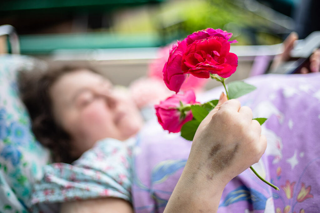 Первый московский хоспис. Женщина с цветком в руке лежит в медицинской кровати