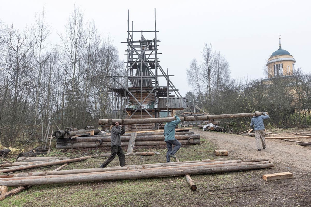 На заднем плане новая часовня, которую мастера и волонтеры построили для музея, на переднем плане переносят бревна отреставрированного амбара-двойни