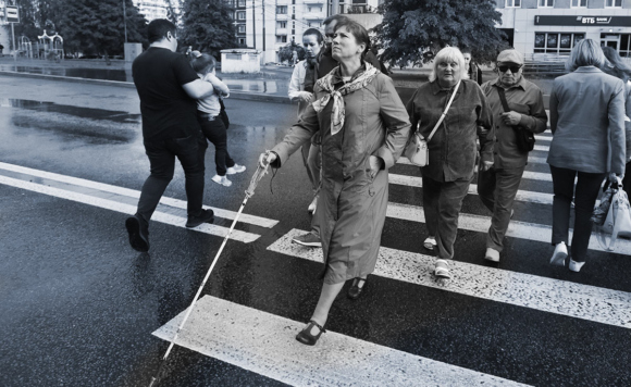 Черно-белая фотография. На первом плане слепая женщина с белой тростью