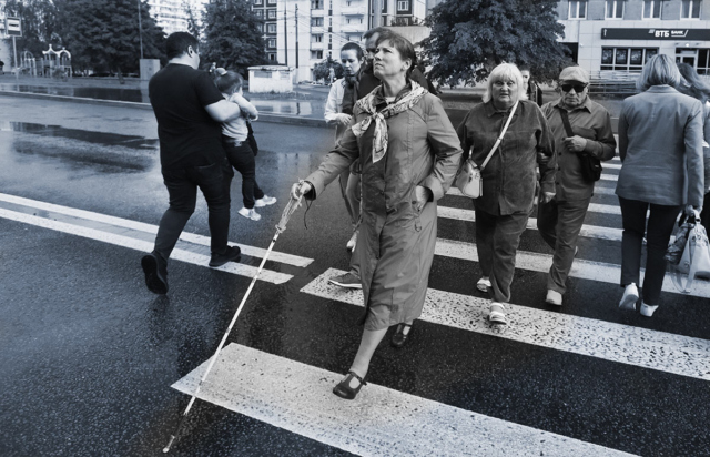 Черно-белая фотография. На первом плане слепая женщина с белой тростью