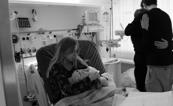 Женщина держит на руках младенца, рядом мужчина и мама