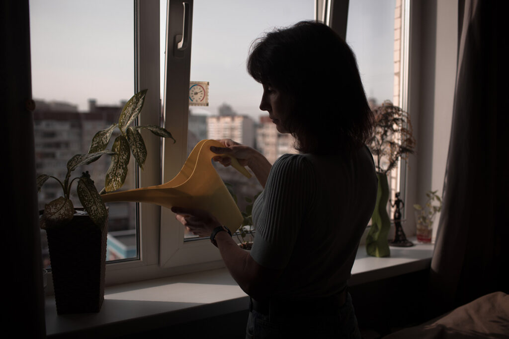 Молодая женщина поливает цветы на подоконнике 