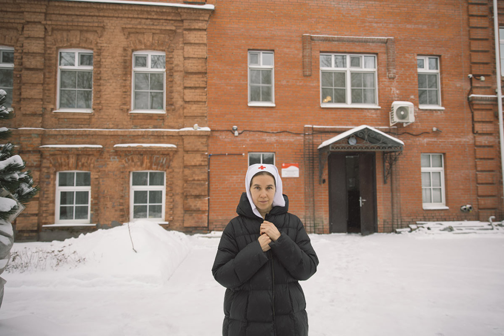 Молодая женщина в платке сестры милосердия на фоне старинного кирпичного здания