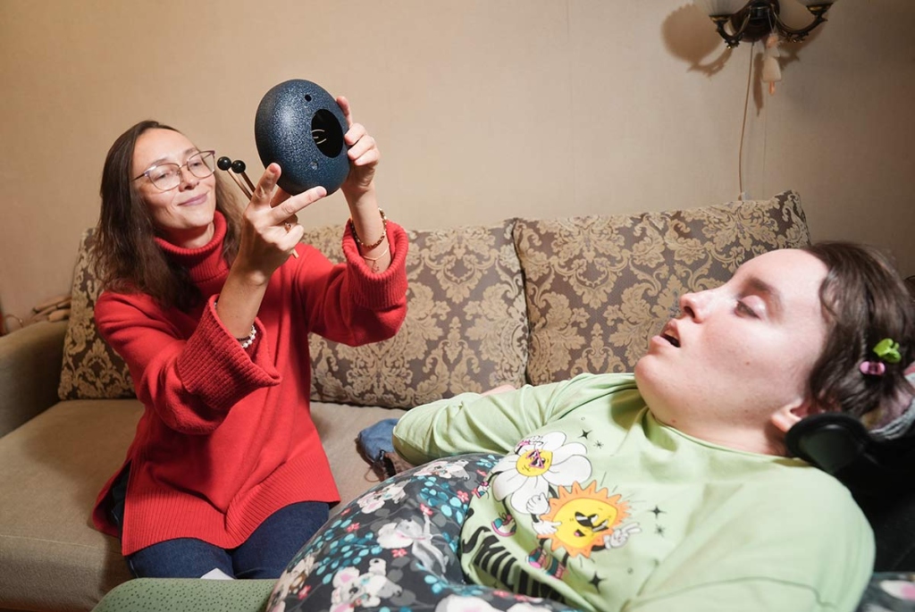 Молодая женщина с музыкальным инструментом и больная девушка в инвалидной коляске