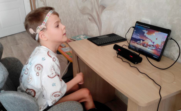 Маленький мальчик с ДЦП смотрит мультики со слуховым аппаратом и айтрекером