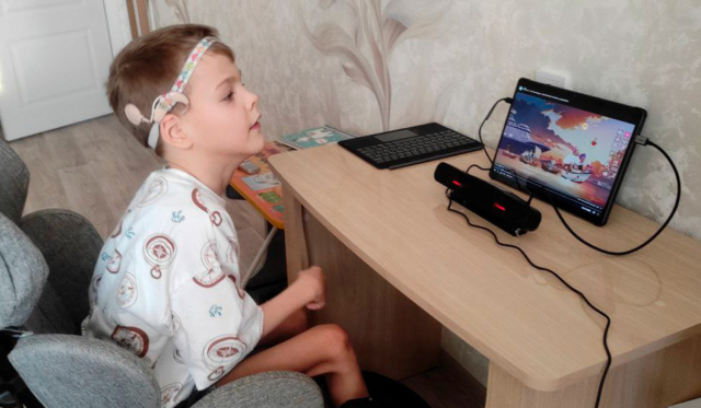 Маленький мальчик с ДЦП смотрит мультики со слуховым аппаратом и айтрекером