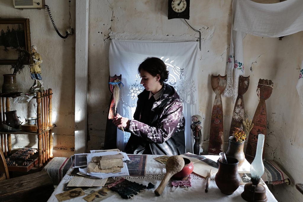 Юноша в старинном деревенском доме, на столе перед ним разные предметы деревенского быта 