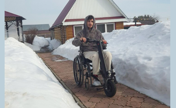 Молодой мужчина на электроколяске на улице на фоне дома