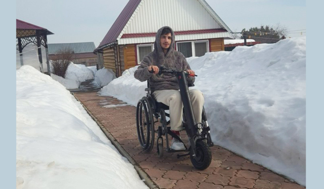 Молодой мужчина на электроколяске на улице на фоне дома